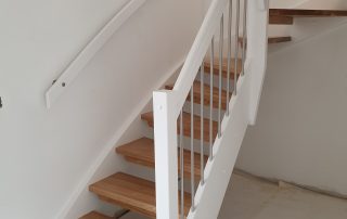 Öppen U-trappa. Steg i lackad ek och sidovang i vitmålat utförande. Räcke i rostfritt stål.