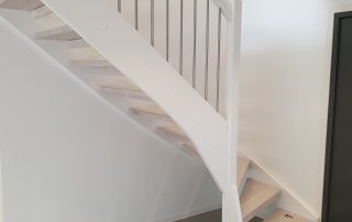 Öppen L-trappa. Steg i vitlackad ek och sidovang i vitmålat utförande. Räcke i rostfritt stål.