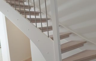 Öppen L-trappa. Steg i vitlackad ek och sidovang i vitmålat utförande. Räcke i rostfritt stål.